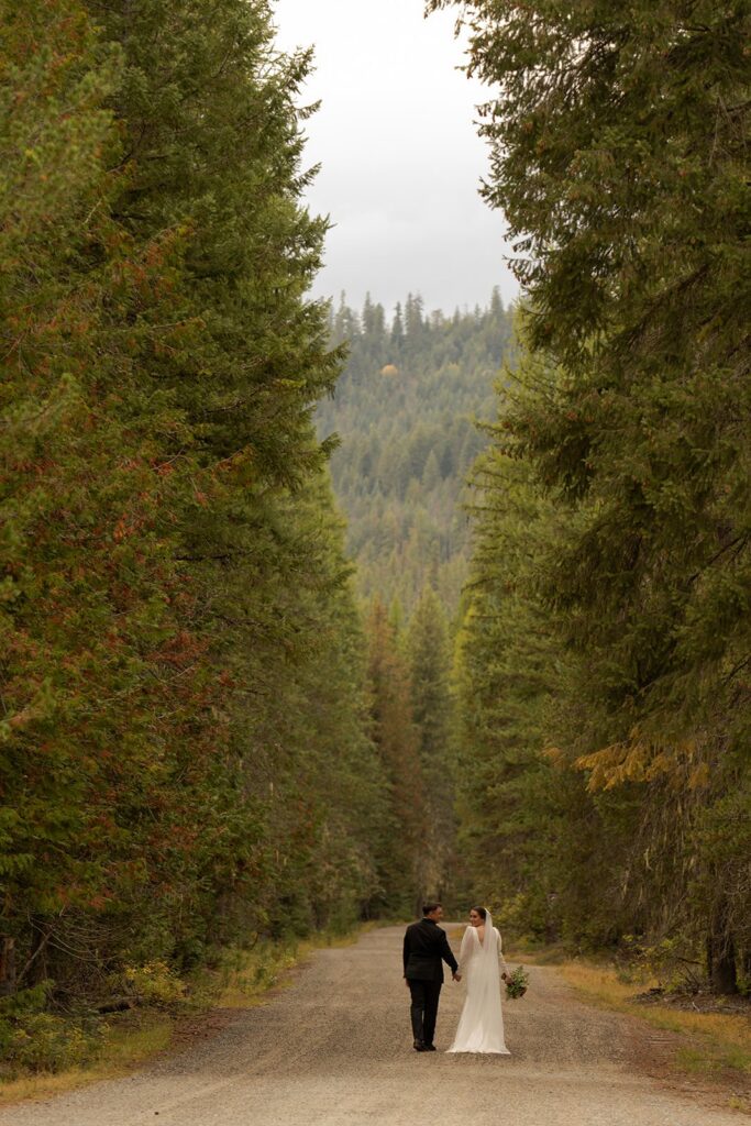Bride and Groom walk down a road through a forest and elope in Idaho