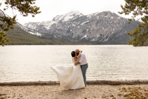 Couple kissing by a mountain lake with sweeping views in one of the best places to elope in Idaho.
