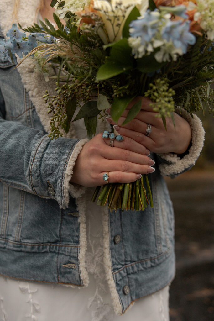 Bride holds her wedding bouquet and wears a jean jacket during her winter Idaho elopement