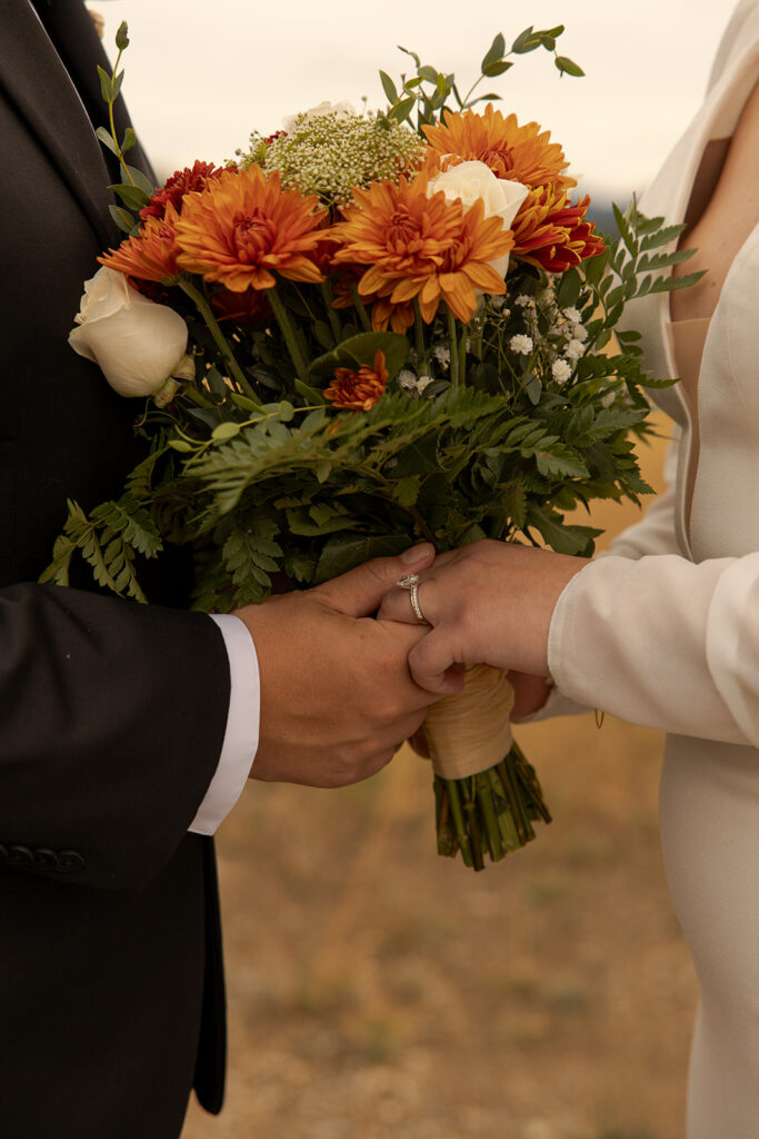 Bride and groom hold each others hands and a bouquet of orange and red flowers during their Idaho elopement