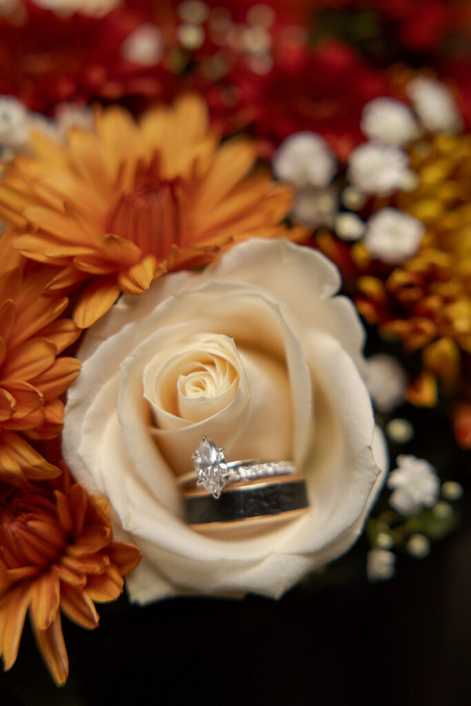 Wedding bands sit inside a white rose surrounded by orange and red flowers at elopements in Idaho