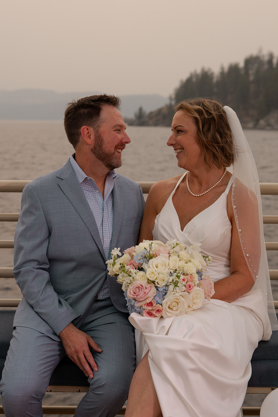 Bride and groom look at each other and smile in front of a lake at their Idaho elopement