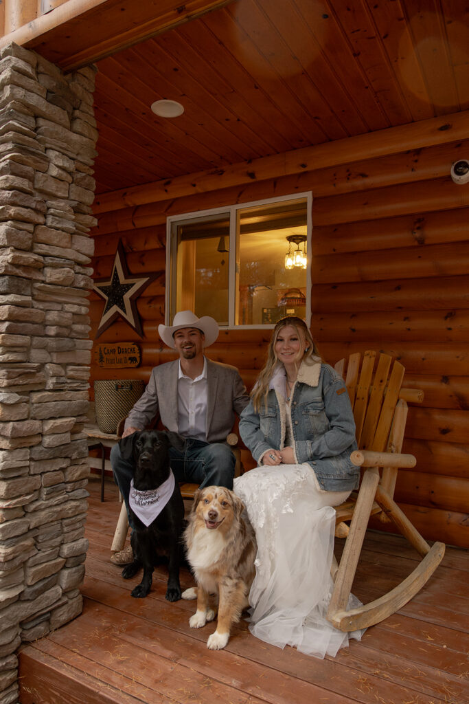 Bride and groom sit in rocking chairs on a porch at a log cabin with their two dogs at their elopement in Idaho