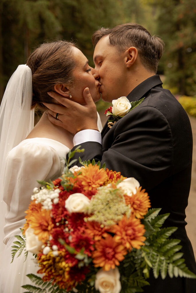 Priest Lake Wedding | Love In The Hills Photo And Video Bride and groom sharing a kiss with their fall bouquet during a Priest Lake Idaho wedding.