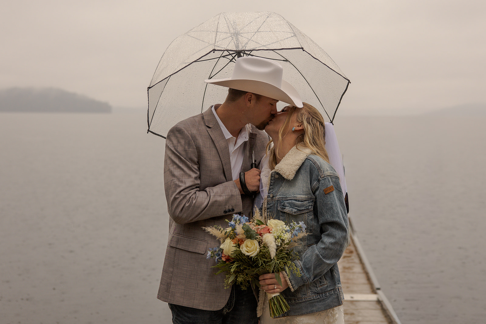 Bride and groom kissing beneath a clear umbrella on a dock during a Priest Lake Idaho wedding.