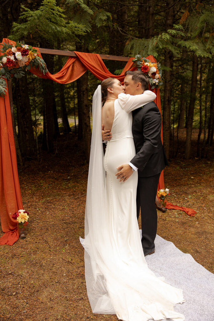 Bride and groom sharing their first kiss during a forest Priest Lake wedding ceremony