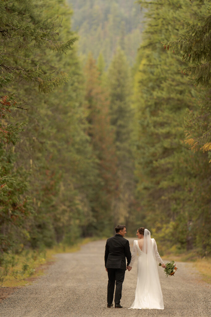 Priest Lake Idaho Wedding | Love In The Hills Photo And Video Bride and groom walking hand in hand down a forest road after their Priest Lake wedding.